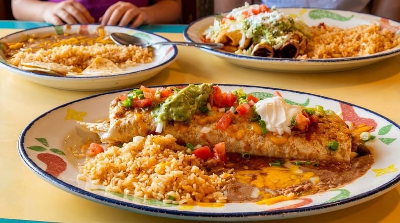 A large burrito with rice, beans, guacamole, sour cream, and salsa on a colorful plate.