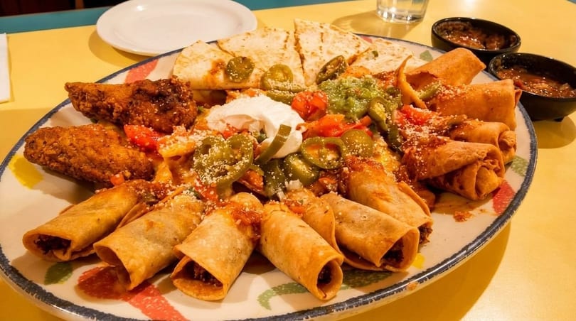 A large platter of Mexican food with taquitos, quesadillas, fried chicken, guacamole, and sour cream.