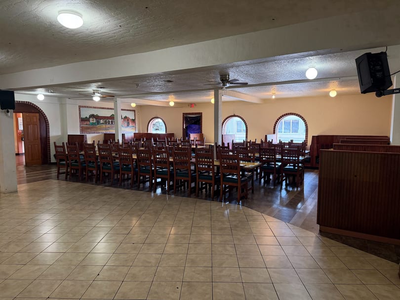 Spacious, empty restaurant dining room with tiled floors, wooden tables and chairs, and arched windows.