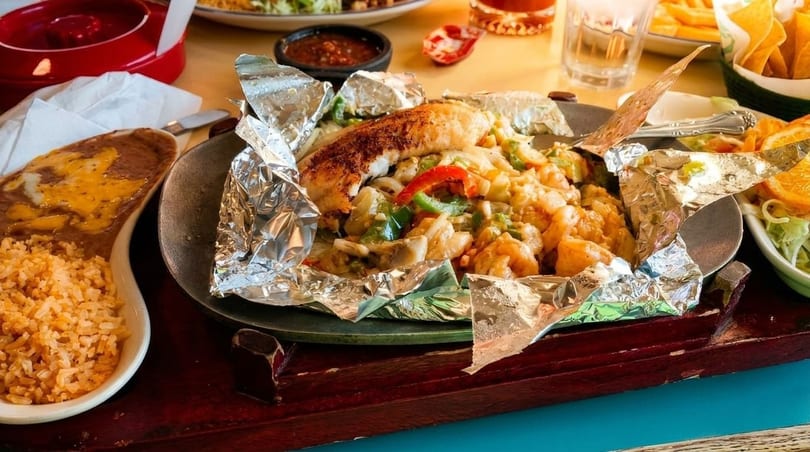 Sizzling fajitas with chicken, shrimp, and vegetables, served with rice and refried beans.