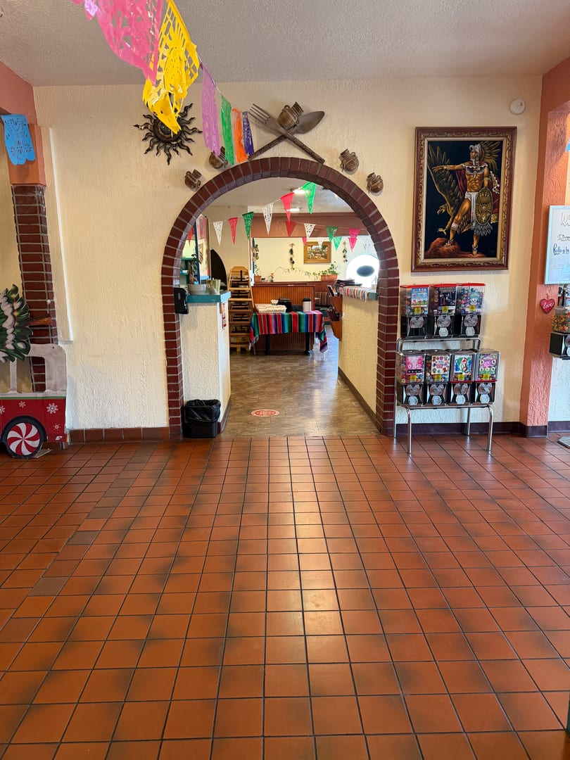 A restaurant entrance with terracotta floor tiles, an arched doorway, and colorful decorations.